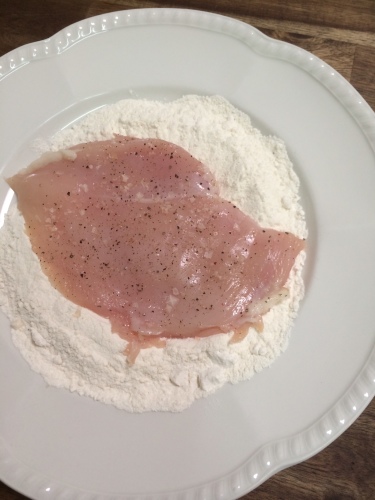 Coating the seasoned flattened chicken breasts in flour
